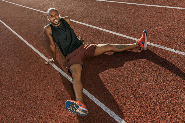 Бегун спортсмен сидит на треке расслабляясь после пробежки в наушниках
 - Фото, изображение
