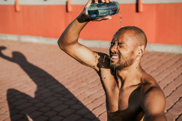 Молодой спортивный мужчина освежает себя водой после тренировок на открытом воздухе
 - Фото, изображение