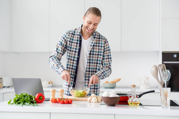 Portrait of his he nice attractive cheerful cheery focused guy making delicious vitamin vegs vegan dinner lunch watching video blog courses classes in modern light white interior style kitchen indoors - Foto, Bild