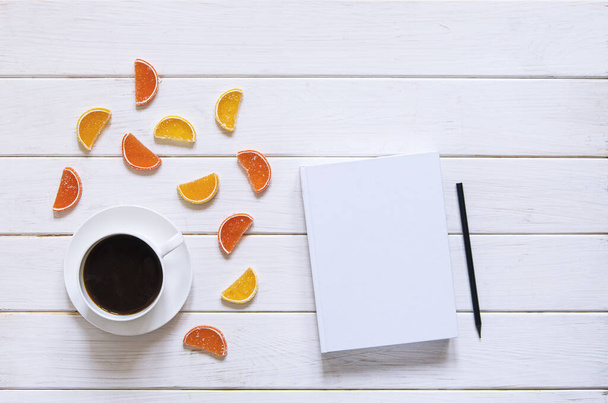 weiße Tasse Kaffee, weißes Papier und bunte Fruchtmarmelade liegen auf weißem Holzgrund. Ansicht von oben - Foto, Bild