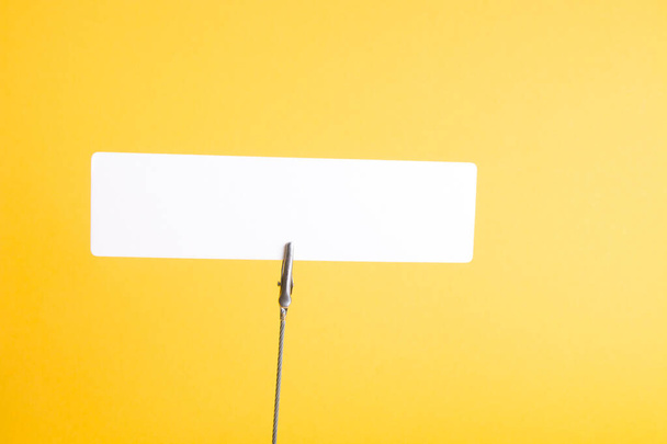 white cardboard rectangle on a clothespin, paper clip on a spring, a reminder on the desktop, copy space, yellow background, place for a title - Photo, Image