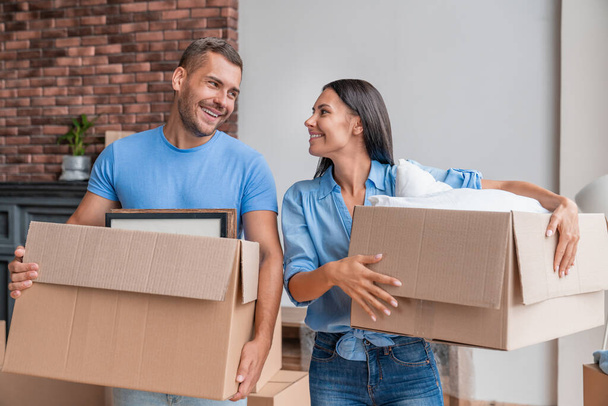 Young family holding cardboard box while moving to new home - Foto, Bild