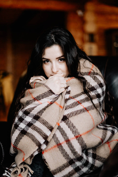 young attractive woman covered with a warm blanket sits on a large chair, wrapped and warmed - Photo, image