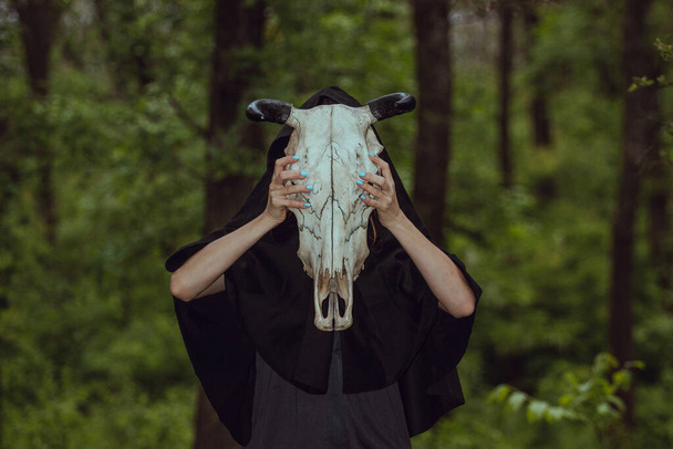 Victim with skull of the animal instead of head. Photo stylized as shooting on an old camera, with noise and imperfection of the image. Woman in forest with skull of cow occupies Occult calls to demon - Photo, Image
