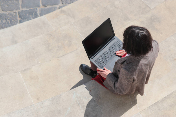 Elegancka bizneswoman siedząca na schodach, pracująca na laptopie, sprawdzająca i odpowiadająca na maile. Technologia, edukacja i koncepcja zdalnej pracy, przestrzeń do kopiowania. Widok z góry - Zdjęcie, obraz