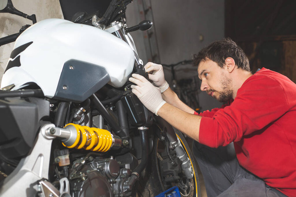 Механик-ремонтник, выполняющий техническое обслуживание или ремонт, фиксирующий на мотоцикле, мотоцикле, сервисном центре
 - Фото, изображение