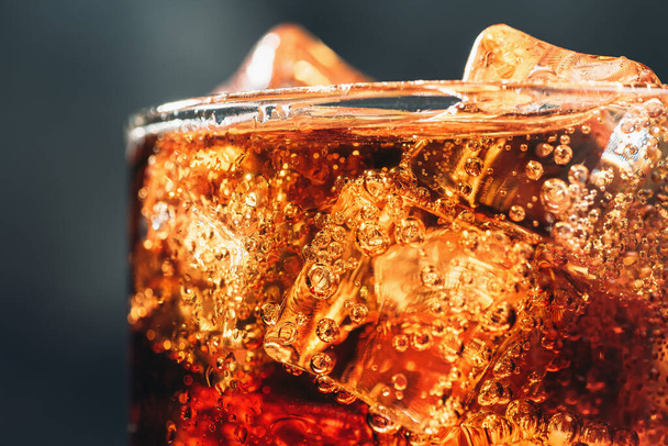 Glass with ice cubes and bubbles of fresh carbonated cola soda drink, macro photo close up - Fotó, kép