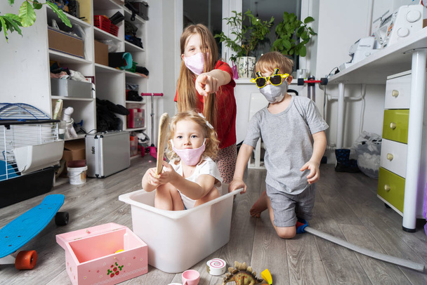 Stay home: Children in medical masks play with toys and ride in a white box. Family lifestyle portrait. - Фото, зображення