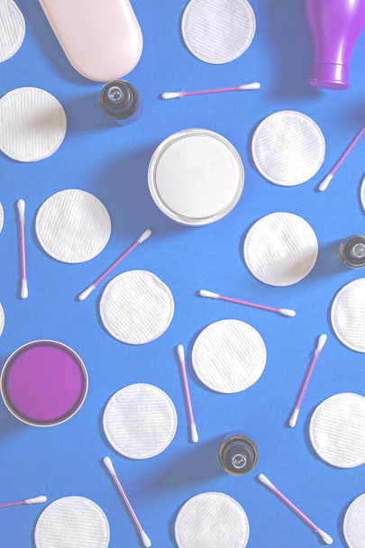Produtos de higiene: almofadas de algodão redondas brancas e varas de plástico para limpar as orelhas encontram-se em um fundo azul ao lado de creme facial. Vista superior, flat lay - Foto, Imagem