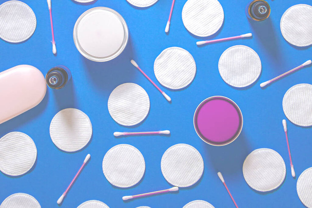 Productos higiénicos: almohadillas redondas de algodón blanco y varillas de plástico para limpiar las orejas se encuentran sobre un fondo azul junto a la crema facial. Vista superior, plano - Foto, Imagen