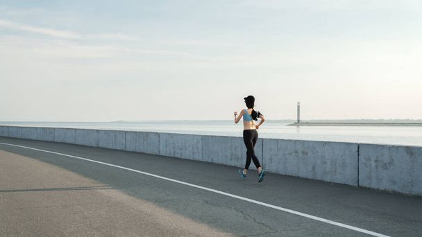 Caucasian female athlete jogging on boardwalk along street. Female runner training outside - Fotoğraf, Görsel