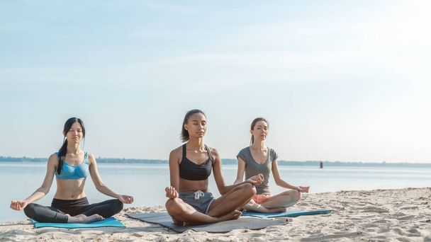 Yoga group sitting and meditates outdoor on the sunny beach - Foto, imagen
