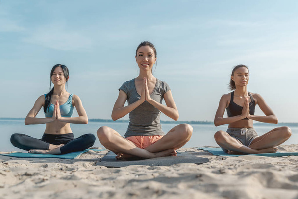 Peaceful girls making yoga meditation in lotus pose on sunny beach - Fotoğraf, Görsel