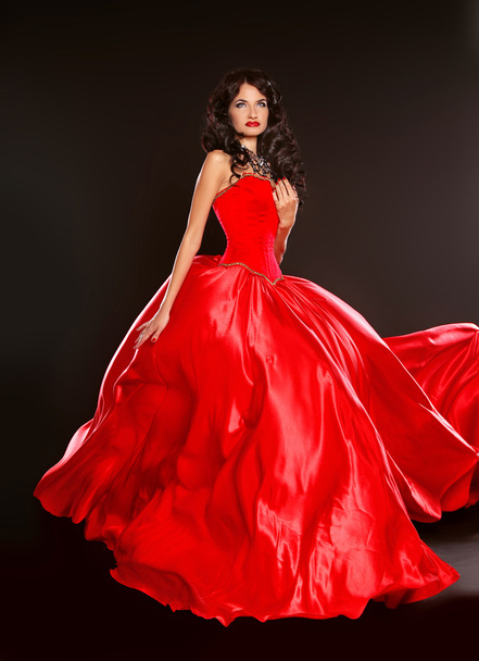 Beautiful brunette wearing in blowing red dress isolated on blac - 写真・画像