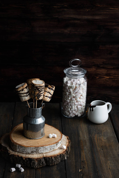 Gebratene Marshmallows auf einem Stock in Schokoladenglasur und garniert mit Graham Cracker. Alternativer Keks-Geruch. Düsterer rustikaler Stil. - Foto, Bild