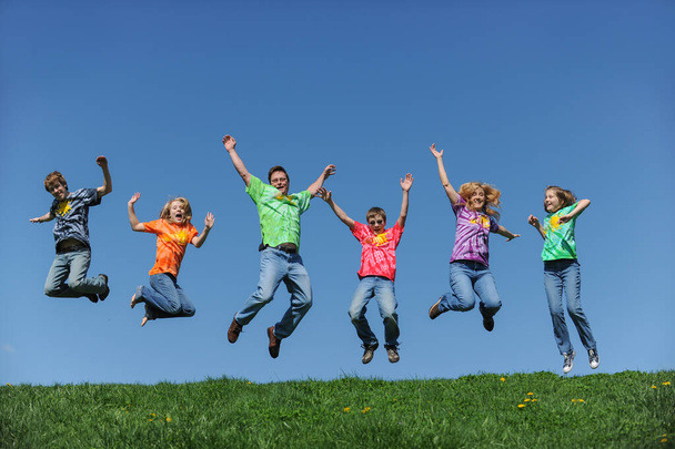 Familie in bunten Shirts hüpft vor blauem Himmel ins Freie - Foto, Bild