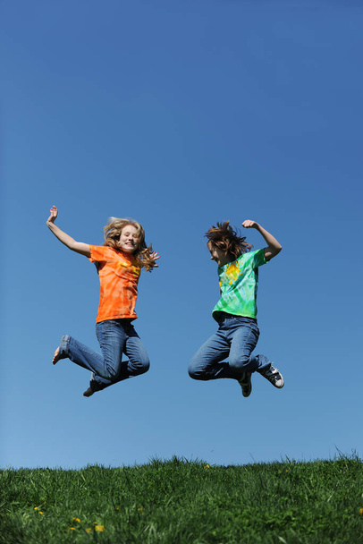 Young girls jumping outdoors against a blue sky on a sunny day - Photo, Image