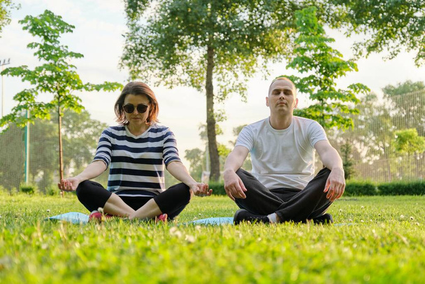 Casal, homem e mulher sentados no parque no tapete em posição de lótus e meditando. Yoga, fitness, estilo de vida saudável ativo em pessoas de meia-idade
 - Foto, Imagem