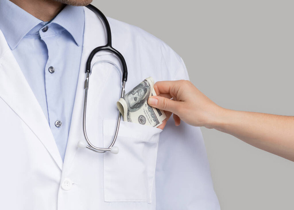 Коррупция в секторе здравоохранения. Неузнаваемый пациент кладет деньги в карман докторов
 - Фото, изображение