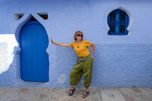 Kaunis nainen hauska poseeraa lähellä vanhan talon julkisivua sinisessä Chefchaouenissa, Marokossa
. - Valokuva, kuva