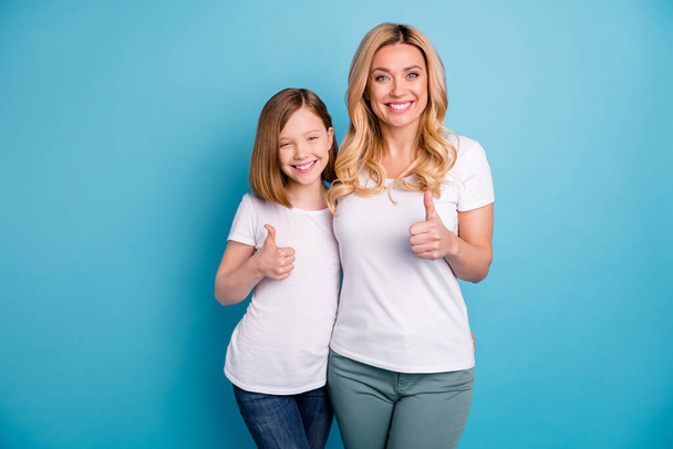 写真2人の魅力的なママの女性の小さな娘を保持親指の指を式の合意を調達陽気な人はカジュアルな白のTシャツを着て隔離された青の色の背景 - 写真・画像