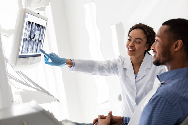 Ystävällinen hammaslääkäri näyttää potilaalle hampaansa röntgenissä
 - Valokuva, kuva