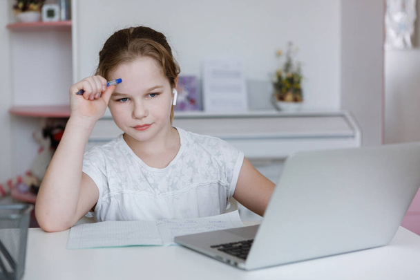 Teenager girl at a table with a laptop and headphones, looks at the camera. Home schooling, social distance. Quarantine coronavirus. Selective focus. Blur background. - Photo, Image