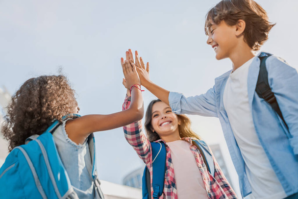 Happy children giving high five each other standing near school outdoors - 写真・画像