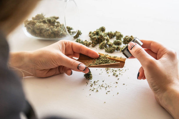Woman preparing and rolling marijuana cannabis joint. Close up of marijuana blunt with grinder. Woman rolling a marijuana blunt on white background. Cannabis use concept. - Foto, Imagen