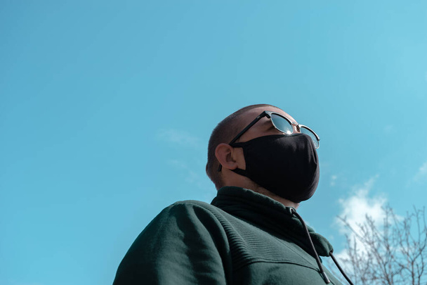 Young man wearing face mask. Handsome man in sunglasses wear black medical mask, sky background, copy space. Pandemic coronavirus covid-19 quarantine period concept - Foto, Imagen
