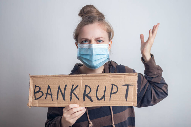 Young caucasian woman girl in mask holding banner bankrupt during coronavirus outbreak - Photo, Image