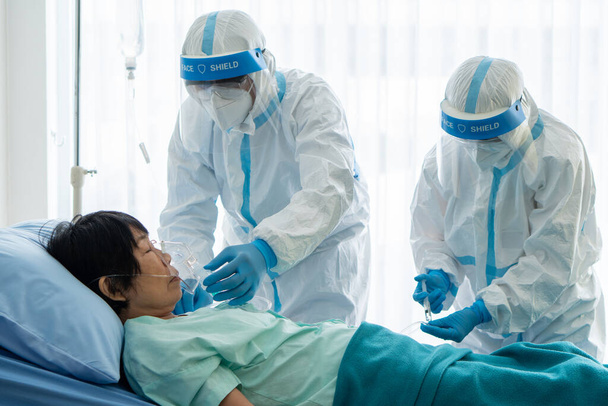 lääkärit henkilökohtaisia suojavarusteita tai ppe antaa happinaamari Aasian nainen potilas covid-19 tai sepelvaltimovirus infektio eristysyksikkö sairaalassa pandemian aikana. lääketieteellinen käsite
 - Valokuva, kuva