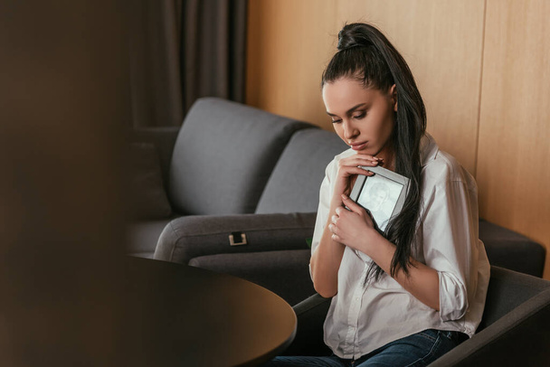 selective focus of depressed young woman holding photo frame near chest - Φωτογραφία, εικόνα