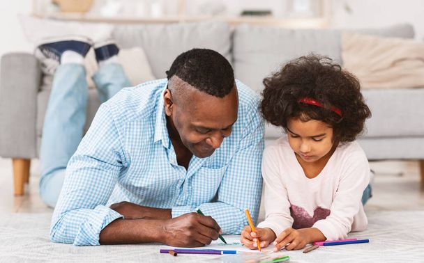 Quiet family times. Pretty African American girl drawing on floor with her granddad - Фото, зображення