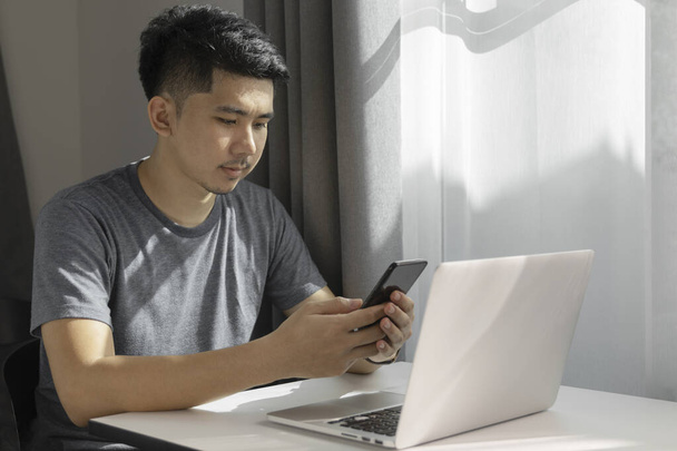 Uomo d'affari che utilizza smart phone inviare messaggi mentre si lavora a casa con il computer portatile
.  - Foto, immagini