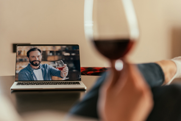 赤ワインのグラスで乾杯するラップトップの画面で女性と若い男のクロップドビュー - 写真・画像