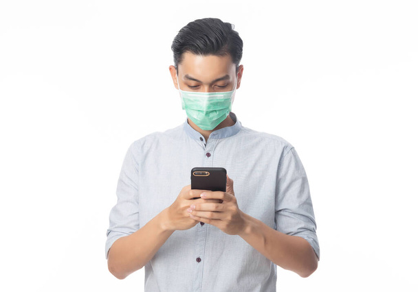 Young Asian businessman in hygienic mask using smartphone, Prevent infection, 2019-nCoV or coronavirus. Airborne respiratory illness such as pm 2.5 fighting and flu. Studio shot isolated on white background. - Zdjęcie, obraz