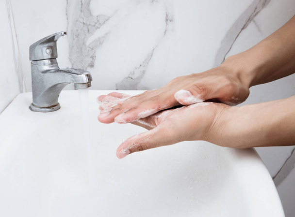 Joven lavándose las manos sobre lavabo en baño, primer plano, virus Corona o prevención Covid-19, higiene para detener
. - Foto, imagen
