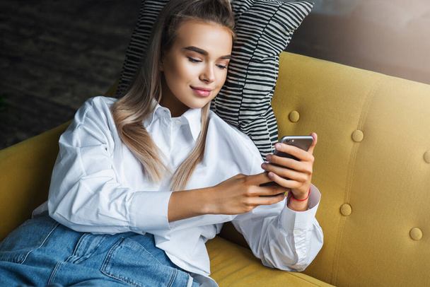 Female relaxing at home, using smartphone to text messages, share photos, communicate with friends, check email - Valokuva, kuva