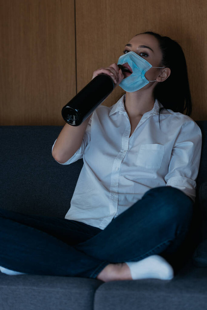 depressed woman in medical mask with hole drinking wine from bottle  - Photo, Image