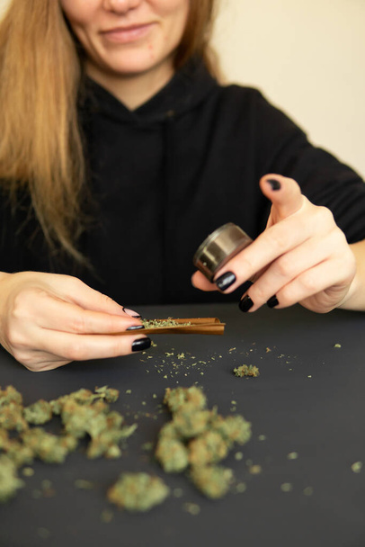 Close up of marijuana blunt with grinder. Marijuana use concept. Woman rolling a marijuana joint. Woman preparing and rolling marijuana cannabis joint. - Photo, Image