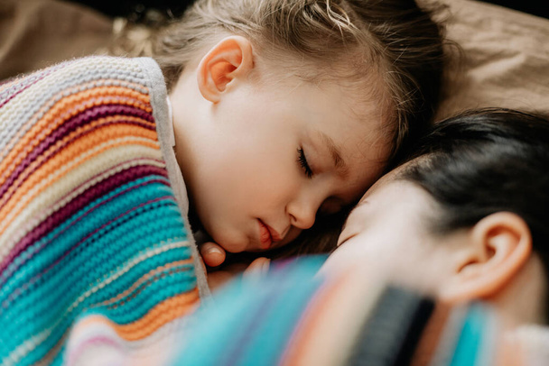 01.06.2019 Vinnytsia, Ukraine: Young mother and baby of 2 years sleep together hugging, daytime sleep concept for children. Mom fell asleep with her baby while putting her to sleep - Foto, Imagen