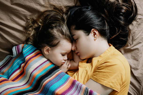 01.06.2019 Vinnytsia, Ukraine: Draufsicht auf eine schöne junge Mutter und ihr süßes kleines Baby, das zu Hause im Bett schläft - Foto, Bild
