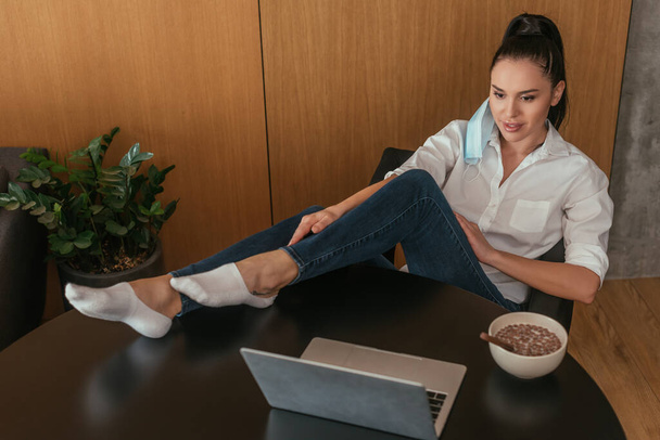 high angle view of young woman looking at laptop near bowl with breakfast on table - Foto, Bild