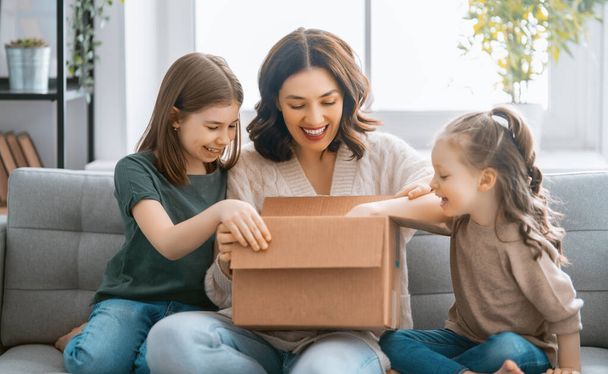 Mother and daughters are unpacking cardboard box at home. - Foto, imagen