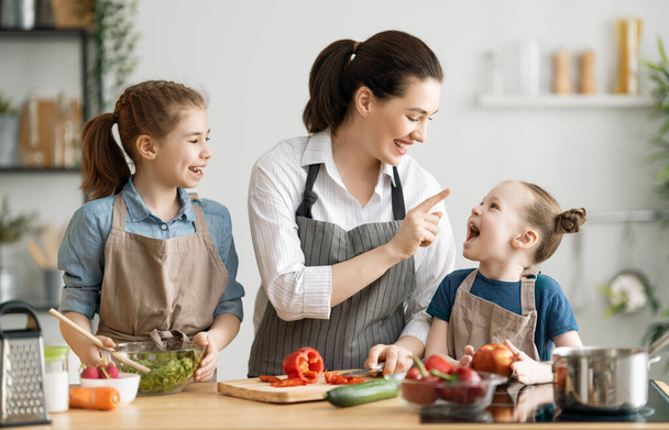Healthy food at home. Happy family in the kitchen. Mother and children daughters are preparing vegetables. - 写真・画像