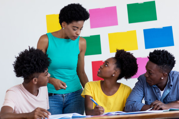 Afrikkalainen amerikkalainen naispuolinen opettaja puhuu oppilaiden kanssa koulun luokassa
 - Valokuva, kuva