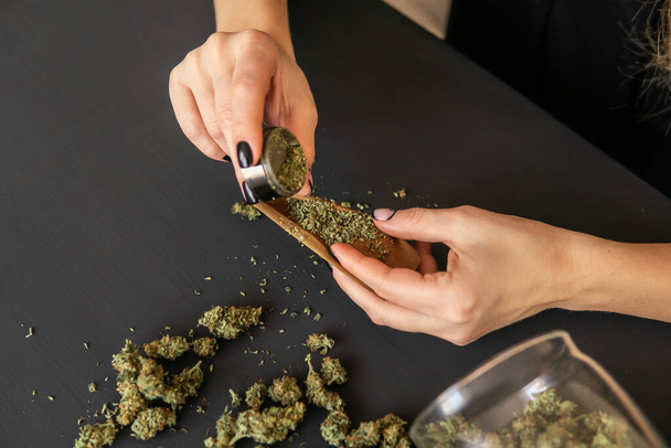 Close up of marijuana blunt with grinder. Marijuana use concept. Woman preparing and rolling marijuana cannabis joint. Woman rolling a marijuana joint. - Photo, Image