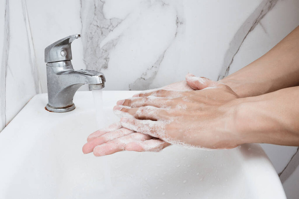 Jongeman handen wassen over wastafel in de badkamer, close-up, Corona virus of Covid-19 preventie, hygiëne te stoppen. - Foto, afbeelding
