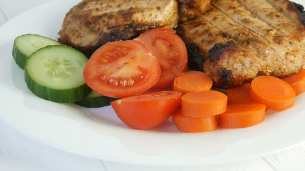Ízletes friss, lédús szeletek grillezett steak entrecote sertéshús mellett cseresznye paradicsom és friss zöldség uborka fehér éttermi tányéron forog - Felvétel, videó